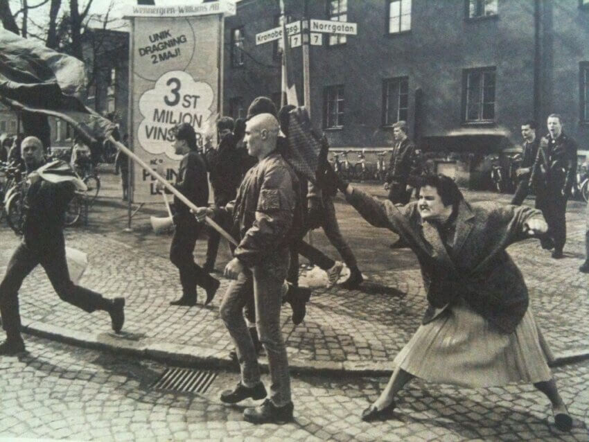 Midaldrende, vred kvinde slår en unge skinhead mand, der demonstrerer med nazi flag